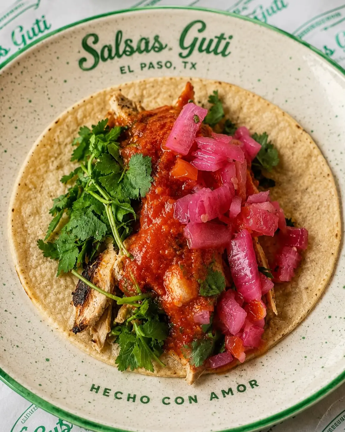 Close-up of a Salsas Guti taco with red salsa, cilantro, and pickled onions